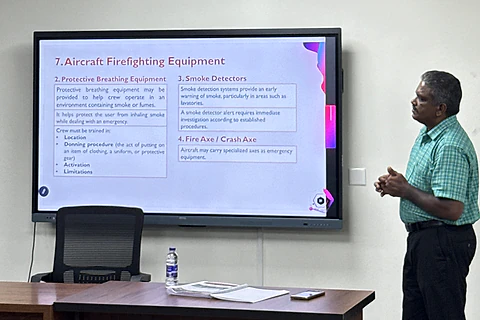A trainer explaining aircraft firefighting equipment beside a presentation screen