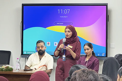 A speaker addressing students with two colleagues seated beside her