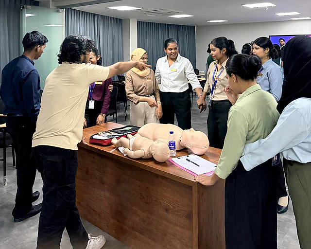Students gathered around a table practising infant first aid on a training manikin